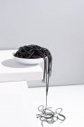 Estúdio minimalista com espaguete de tinta de lula preta caindo da tigela de cerâmica completa na mesa branca — Fotografia de Stock