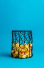 Set of cute rubber ducklings toys placed inside wire basket on bright blue background — Stock Photo