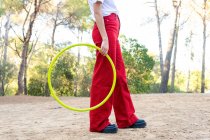 Вид збоку врожаю невпізнаваної жінки-підлітка в червоних джинсах, що тримає обруч, при цьому проводячи вільний час у парку — стокове фото