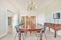 Interno della spaziosa sala da pranzo luminosa con tavolo e sedie in legno vicino al tavolo antico con lampada — Foto stock