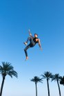 De baixo vista lateral do atleta enérgico no desgaste da moda realizando truque contra o céu azul na luz solar — Fotografia de Stock