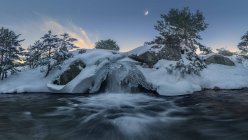 Lange Belichtung des schnellen Wasserfalls, der durch schneebedecktes Gelände im Sierra de Guadarrama Nationalpark fließt — Stockfoto