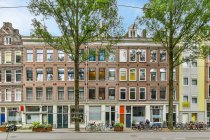 Aged house exterior against roadway and parked bikes between overgrown trees in daytime in Amsterdam Holland — Stock Photo