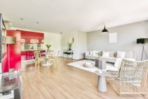 Wohnbereich mit bequemem Sofa und Sessel und Küche mit roten Möbeln in zeitgenössischer offener Wohnung — Stockfoto