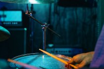 Обрезанный неузнаваемый концентрированный мужчина-музыкант, играющий на барабанах в клубе с зеленой и синей неоновой подсветкой — стоковое фото