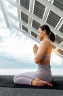 Full body side view of tranquil female with closed eyes in activewear doing namaste gesture with folded hands on street near solar panel — Stock Photo