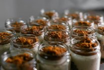 De arriba frascos de vidrio con delicioso postre de capa con crema blanca decorada con cobertura de caramelo y nueces trituradas servidas en la mesa en la cocina - foto de stock