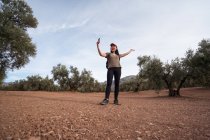 Розсудливий азіатський мандрівник з широкими руками робить автопортрет на смартфоні, стоячи на плантації з оливковими деревами в сільській місцевості. — стокове фото