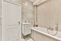 Quarto de banho contemporâneo interior com banheira e parede de azulejos cinza contra lavatório em casa de luz — Fotografia de Stock