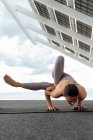 Corps complet de femme forte pieds nus en vêtements de sport pratiquant la posture Maksikanagasana dans la rue près du panneau photovoltaïque pendant l'entraînement de yoga en ville — Photo de stock