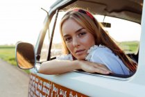 Симпатична блондинка сидить всередині старовинного фургона і спирається на вікно в сонячний день — стокове фото