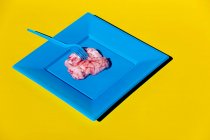 Heap de cérebros crus rosa servido em placa azul com garfo de plástico no fundo amarelo no estúdio criativo moderno claro — Fotografia de Stock
