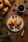 Dall'alto di croissant al forno freschi saporiti serviti su piatto con frutta messa vicino a tazza di tè su tavolo di legno in tempo del mattino in camera leggera — Foto stock