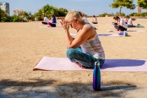 Seitenansicht einer ruhigen Frau mit kurzen Haaren in Aktivkleidung, die Padmasana mit Namaste-Händen macht, während sie bei sonnigem Wetter im Freien auf einer Yogamatte sitzt — Stockfoto