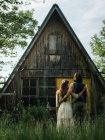 Vista trasera de una atractiva pareja abrazándose frente a una vieja casa de madera desde arriba - foto de stock