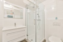 Interno del moderno bagno luminoso con cabina doccia e servizi igienici vicino lavabo sotto specchio in appartamento — Foto stock