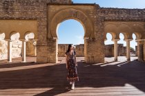 Corpo cheio de viajante asiático feminino em pé perto de pedra pórtico antigo com colunas e passagens arqueadas durante a viagem na cidade de Córdoba — Fotografia de Stock