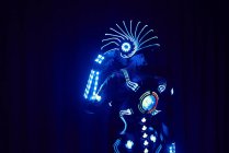Persona senza volto in abito luminoso contemporaneo di cyborg spaziale con illuminazione al neon e casco in piedi su sfondo nero in studio scuro — Foto stock