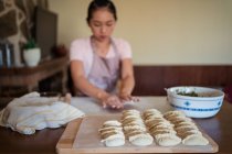 Femmina in grembiule rotolando pasta con le mani sul tavolo mentre prepara gnocchi fatti in casa in cucina — Foto stock