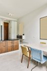 Sedie colorate a tavola vicino a armadi in legno e mensola in elegante cucina con lampada in appartamento — Foto stock