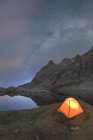 Vue panoramique de la tente sur la rive du lac contre la montagne enneigée sous le ciel nuageux de la voie lactée dans la soirée situé dans Circo de Gredos cirque en Espagne — Photo de stock