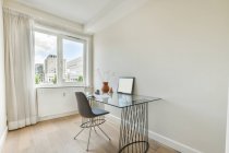 Glastisch mit Dekoration und Stuhl neben Fenster mit Vorhang im sonnenbeschienenen Home Office — Stockfoto