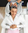 Cultive o mestre irreconhecível que lava o cabelo escuro do cliente feminino com olhos fechados no salão de beleza — Fotografia de Stock