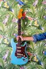 Unerkennbarer Erntemusiker zeigt E-Gitarre gegen lebhafte Bilder von Blättern und Papageien an der Wand — Stockfoto