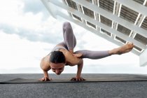 Full body of strong barefoot female in sportswear practicing Maksikanagasana posture on street near photovoltaic panel during yoga training in city — Stock Photo