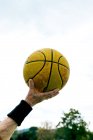 Анонимный взрослый человек с желтым баскетбольным мячом в руке, стоящий на общественной спортивной площадке во время игры на улице — стоковое фото