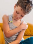 Kranker Junge misst Temperatur mit elektronischem Thermometer, während er zu Hause auf der Couch sitzt und Grippe hat — Stockfoto