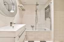 Керамічний умивальник під дзеркалом проти душу і ванни в сучасній ванній кімнаті з плиткою в будинку — стокове фото