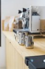 Soft focus of stainless professional pitchers for pouring milk placed on wooden counter in modern coffee house with coffeemaker machines — Stock Photo