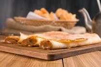 Frisch gerollte Crêpes gefüllt mit süßer Dulce de leche-Füllung, serviert auf einem Holzbrett auf einem Tisch mit Wasserkocher in der Küche — Stockfoto