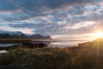 Дивовижний краєвид спокійного озера, оточеного скелястими горами з сніжними вершинами під мальовничим хмарним небом заходячого сонця в Ісландії. — стокове фото