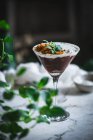 Glas süße Mousse mit Schokolade und Kokosnuss garniert mit Minzblättern und auf den Tisch mit grünen Pflanzen gestellt — Stockfoto