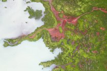 Drone view of rough rocky brown formations surrounded by lush green plants covered with thick fog in nature of Iceland — Stock Photo