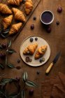 De cima de croissants frescos saborosos cozidos no forno servidos na chapa com frutos colocados perto da xícara do chá na mesa de madeira no tempo da manhã na sala clara — Fotografia de Stock