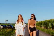 Дві щасливі подруги, одягнені в літній одяг, розважаються над вінтажним фургоном в сонячний день — стокове фото
