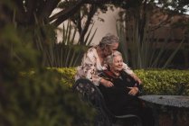 Glücklich gealterte Frau umarmt und küsst Schwester auf den Kopf dann lächelnd, während sie Zeit im Garten zusammen verbringen — Stockfoto