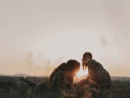 Пара хиппи в солнечных очках, лежащих на травянистом лугу на природе, наблюдая за закатом среди гор — стоковое фото