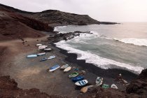 Drone view of boats on Ciclos Beach against foamy ocean and Guincho Volcano in Golfo Yaiza Lanzarote Canary Islands Spain — стокове фото