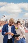 Jovem macho com copo de suco de laranja em pé perto de fêmea flatmate comer maçã verde saudável no telhado e tablet de navegação juntos — Fotografia de Stock
