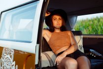 Menina morena atraente com chapéu dentro de uma van vintage e deitada no assento em um dia ensolarado — Fotografia de Stock