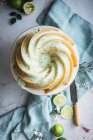 Vue de dessus du délicieux gâteau au citron vert servi sur une assiette blanche près des fleurs et des tranches de citron vert — Photo de stock