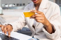 Crop mujer anónima con tarjeta de crédito en la mano escribiendo en netbook moderno al hacer la compra en línea en la calle en la ciudad - foto de stock