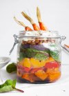 Салат с разноцветным спелым перцем и булгуром, увенчанным сырой морковью, подаваемой в банке на белом фоне — стоковое фото