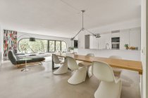 Moderne Raum- und Kücheneinrichtung mit Sofa und Tisch unter Lampen gegen Fenster und Bücherregal im Haus — Stockfoto