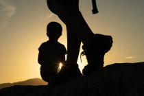 Силует ніг жінки, яка ходить по горах зі своїм сином і сонцем, створюючи сонячну зірку на заході сонця — стокове фото
