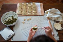From above of crop unrecognizable woman in casual clothes and apron stuffing dumplings with meat while preparing traditional Chinese jiaozi in kitchen — Stock Photo